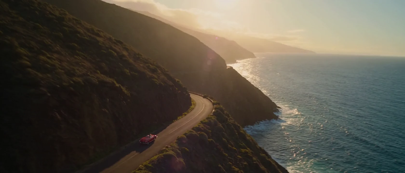 A red vintage convertible on a coastal road in golden light